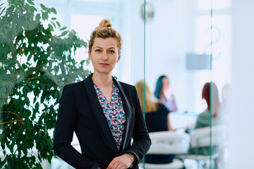 Portrait of a Blonde Businesswoman in a Modern Office with Her Workspace and Colleagues in the...