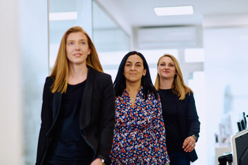 Confident businesswomen stride through the office hallway, deep in discussion.