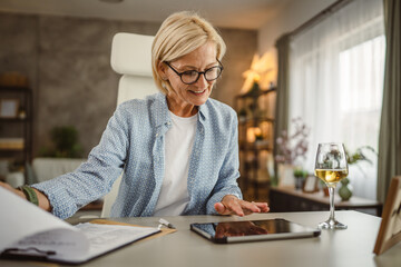 Mature woman work from home analysis document on clipboard and tablet