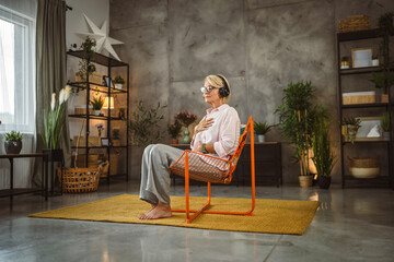 Mature woman sit on chair with headphones and have guided meditation