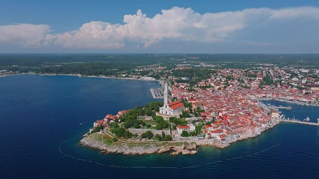 Rovinj, Croatia - 4K flying around the Church of St. Euphemia at the Old Town of Rovinj on a hot summer day with red rooftops, blue sky and clouds at background