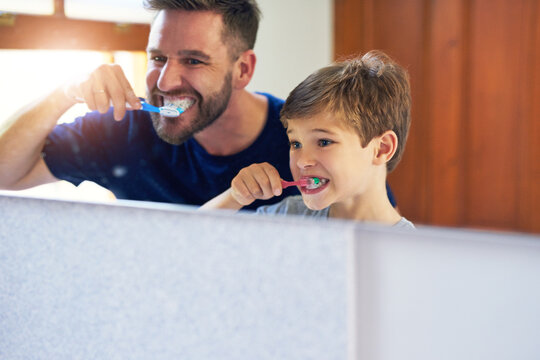 Father, family and kid brushing teeth in mirror with dental hygiene, cleaning and support at home. Dad, man or parent with boy or child learning of mouth and oral health with toothpaste in bathroom