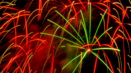 Beautiful close-up background photo of blurred exploding green and red fireworks against a black night sky background.