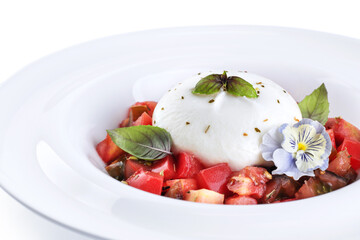 Burrata cheese with tomatoes, edible flower and basil, on a plate on a white background.