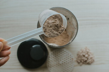 woman pours a measuring cup of chocolate protein into a shake to make a shake for athletes