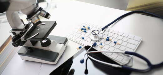 Close-up of doctor desk with mess and chaos on surface, stethoscope tool, scattered pills on keyboard, black tablet screen. Messy, medicine, office concept