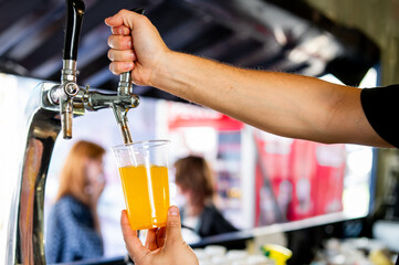 A hand pours beer from a tap into a clear plastic cup at a bar or public event.