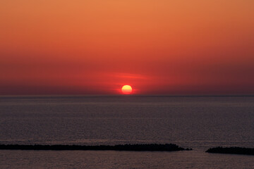 新潟の春の海に沈む少し霞んだ丸い太陽と真っ赤な美しい夕焼け