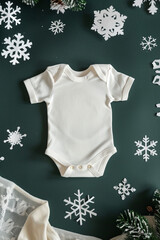 White cotton baby bodysuit onesie with paper snowflakes and evergreen tree branches on dark green modern background with copy space, Winter pregnancy announcement mockup template, Generative AI