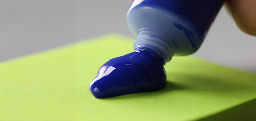 Close-up of man artist squeeze paint out of tube, bright blue colour on green paper. Tool for...