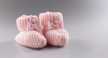 Close-up of pair of knitted pink baby booties with cute bow on it. Handicraft shoes for newborn baby on grey surface. Handmade, crochet, wool, care concept