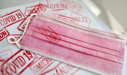Obraz premium Pink medical mask with omicron print. Different new stamps coronavirus infection concept