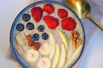 Bowl filled with healthy smoothie, fruit pieces and nuts on the table. Flat lay.
