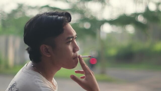 Southeast Asian man smoking with a blurred background or bokeh effect. Slow-motion shot footage.
