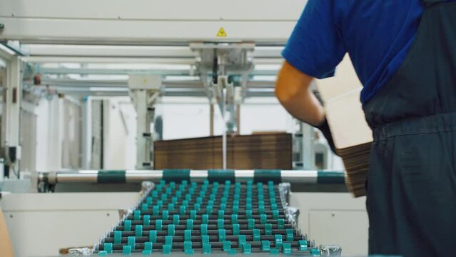 Conveyor line for production of corrugated cardboard boxes. Line for production of brown cardboard boxes. Modern factory, cardboard box from recycled paper. Worker folds finished packaging, close-up.