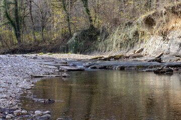 A shallow riverbed with an exposed rocky bottom, a small stream and a flow of water, autumn in nature