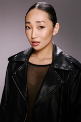 Asian woman, black leather jacket, posing, camera, gray background a stylish asian woman is striking a pose in a black leather jacket, capturing the attention of the camera against a neutral gray