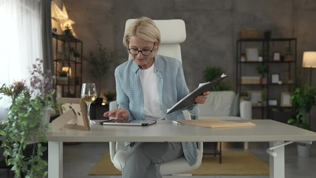 Mature woman work from home analysis document on clipboard and tablet
