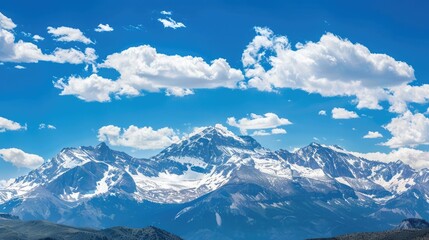 Panoramic view of snow-capped mountains against a blue sky with fluffy clouds.
