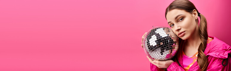 Young woman in 20s holding disco ball in front of her face, creating a whimsical and mysterious spectacle against pink backdrop.