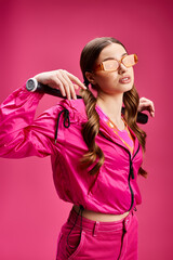 Young beautiful woman in her 20s wearing a pink jacket and pink pants, striking a pose in a studio...