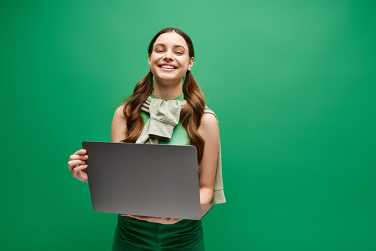 A woman in her 20s holding a laptop in front of a vibrant green background, exuding digital empowerment and connection.