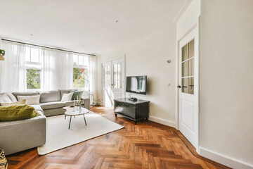 A bright, airy living room featuring large windows, hardwood flooring, and comfortable modern furnishings under warm daylight.