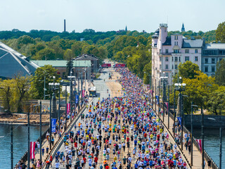 Aerial shot of marathon in Riga, Latvia. Runners spread across a bridge with the city skyline,...