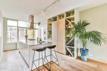Bar stools at counter placed near cabinets and modern appliances in light stylish kitchen with...