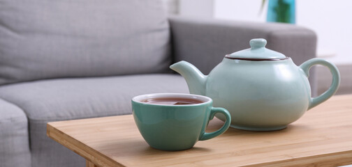 Teapot and cup of hot tea on table in living room