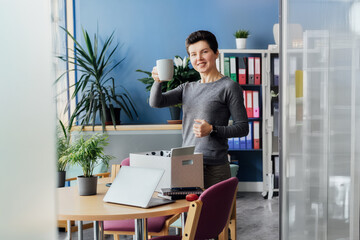 Satisfied newcomer middle aged neutral gender female company worker standing in office unpacking...
