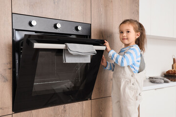 Cute little girl opening electric oven in kitchen. Child at risk