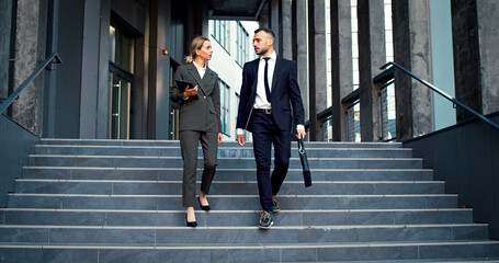 Couple of managers go downstairs business center. People wearing business suits speak on way home...