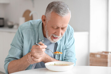 Senior man suffering from Parkinson syndrome eating at table in kitchen