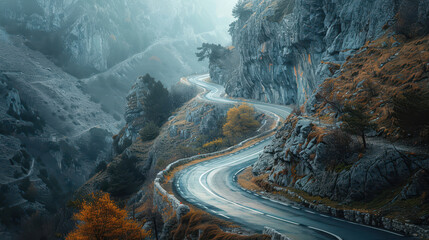Winding mountain road amid rocky terrain and autumn foliage in misty weather