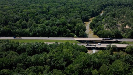 Cars and trucks in traffic traveling on interstate highway through green landscape with trees and...