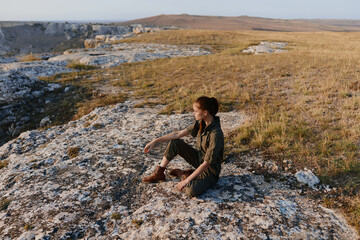 Woman enjoying serene moment on top of rock in vibrant grass field, tranquil travel escape in nature beauty