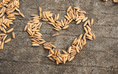 Unhulled rice grains are spread out on a dark-colored mesh surface, forming the shape of a heart.