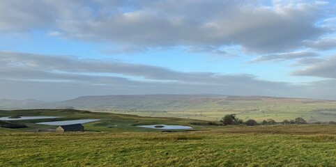 Panoramic view as green fields stretch into the distance, merging with mist and rain showers that shroud the Yorkshire Dales hills on a cold winters day high above, Silsden, Keighley, UK