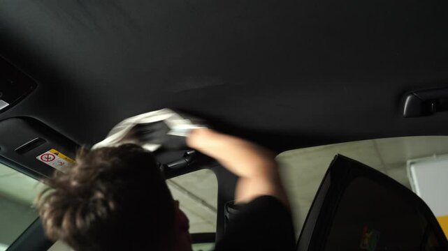 4k video detailing car headliner covering. Spraying detergent on the headliner in car. Hand cleans car ceiling with detergent and microfiber rug.