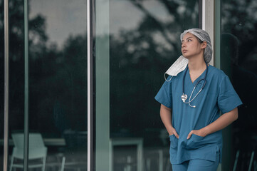 Tired depressed female asian scrub nurse wears face mask blue uniform sits on hospital floor,Young...