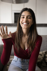 Positive beautiful young adult Indian influencer girl waving greeting hand, looking at camera,...