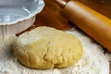 Making a pie.  Getting ready to make a pie.  Dough on a floured wooden surface.  Pie plate and wooden rolling pin in background.