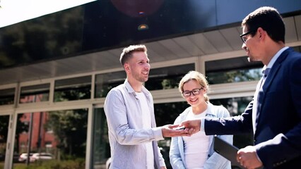 Young salesman selling a new car to a couple by handing over the key