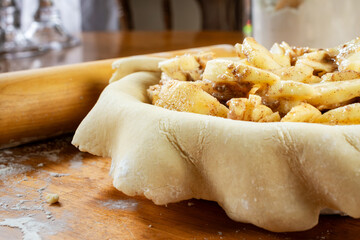 Making a pie.   Rolled dough placed over a pie shell and filled with sliced apple filling.  Side view.  Flour canister and rolling pin in background.