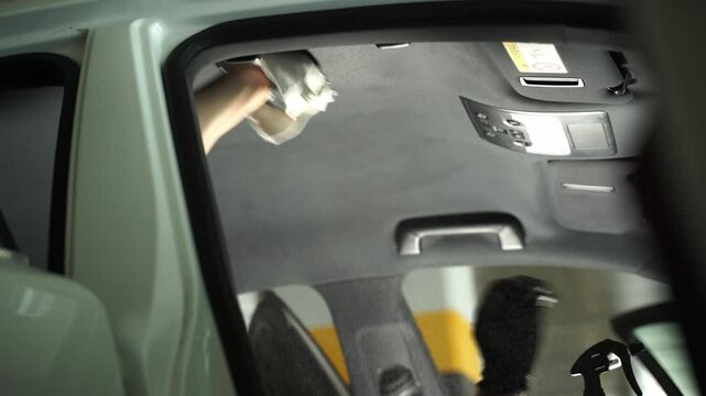 4k video spraying detergent on the headliner in car. Hand cleans car ceiling with detergent and microfiber rug. Detailing car headliner covering.