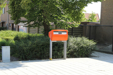 an orange public mail box of dutch postal company PostNL in a public space in a village in the netherlands