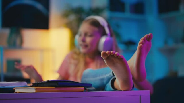 Girl listening to music in headphones while studying, sitting barefoot at desk