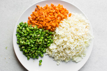 Overhead view of diced carrots green beans and shredded cabbage on a white plate, top view of sliced carrots haricot vert and cabbage on a marble countertop