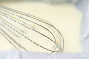 A whisk is sitting in the dough in a loaf tin with a sheet of parchment paper